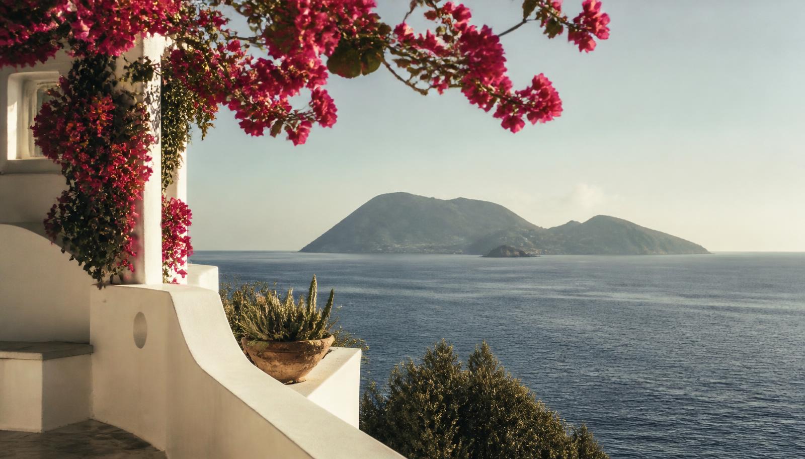 Whitewashed Aeolian terrace with bougainvillea overlooking the sea and a volcanic island at golden hour