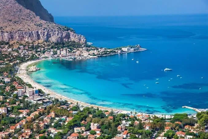 Panoramic view of the turquoise bay and sandy coastline framed by coastal cliffs in Mondello, Sicily.