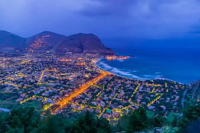: Golden hour sunset casting warm reflections over the calm sea and sandy beach in Mondello, Sicily.