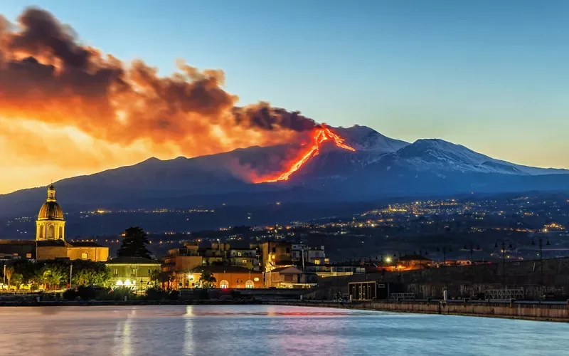 Picturesque landscape view of lush foothills and countryside with Mount Etna in the background.