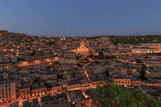 Warm golden hour sunlight illuminating the historic limestone buildings and rooftops of Modica.