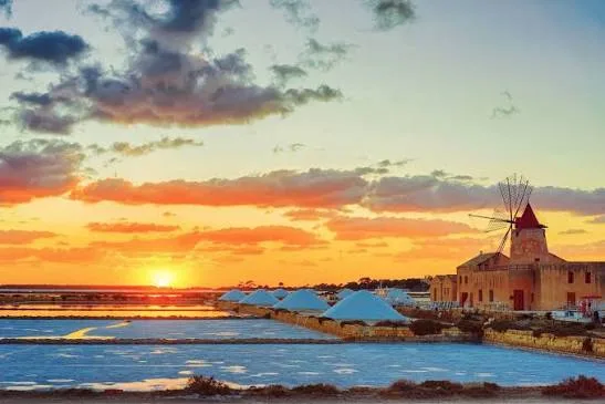 Warm golden hour sunlight illuminating the historic seaside promenade and coastline in Trapani, Sicily.