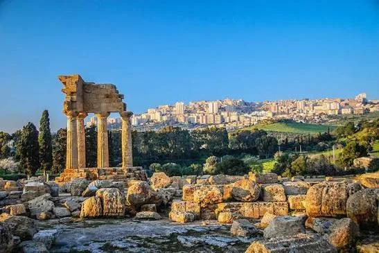 Warm golden hour sunlight illuminating the historic hillside ruins and olive groves in the Valley of the Temples, Agrigento.